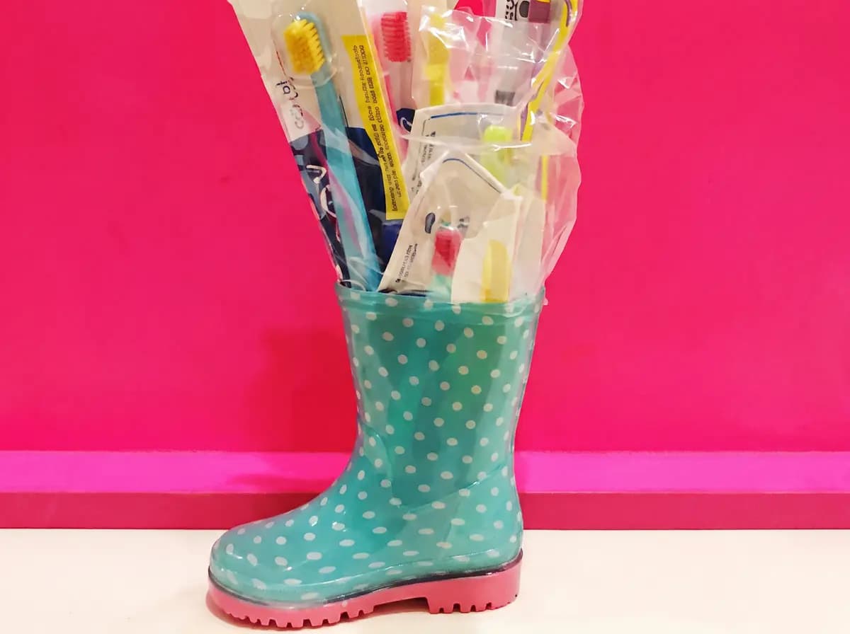 Türkiser Gummistiefel gefüllt mit verpackten Zahnbürsten vor pinker Wand